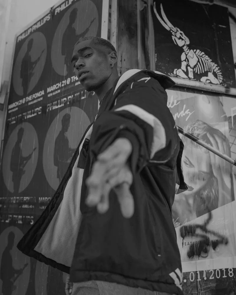Model in a dark hardshell jacket against a pasted poster wall