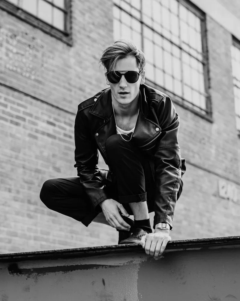 Model crouched on a rooftop in a black jacket and sunglasses