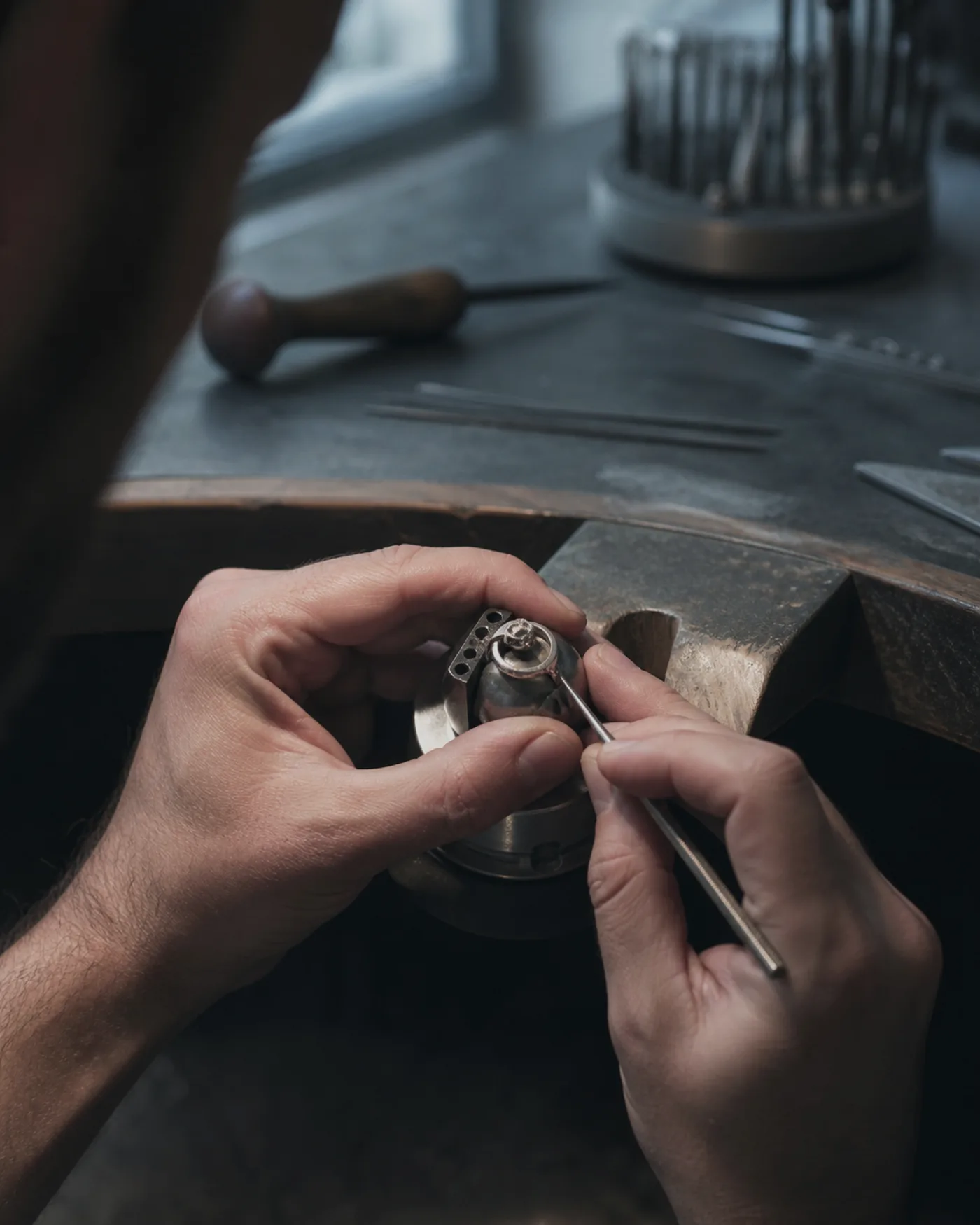 A jeweller's bench with hand tools, wax models and a part finished platinum cuff under a task lamp.