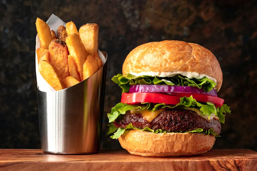 A cheeseburger and a steel cup of fries on a serving board