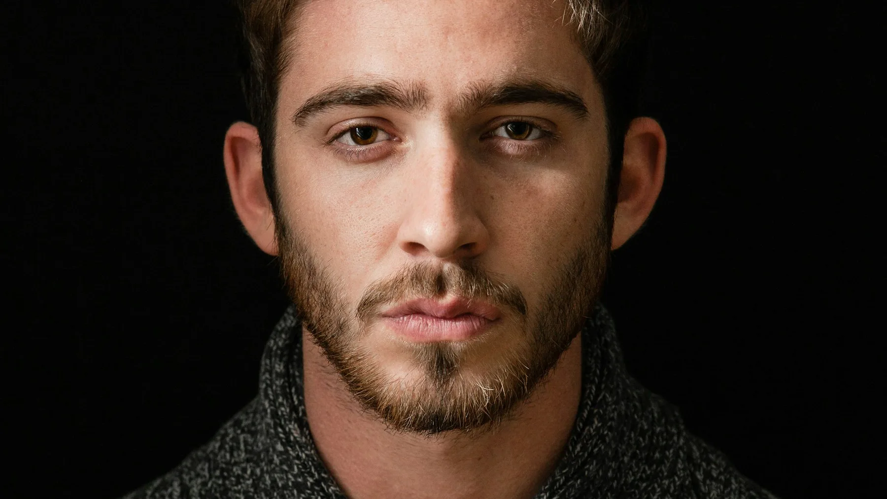 Studio portrait of a bearded man lit from the side against a black background