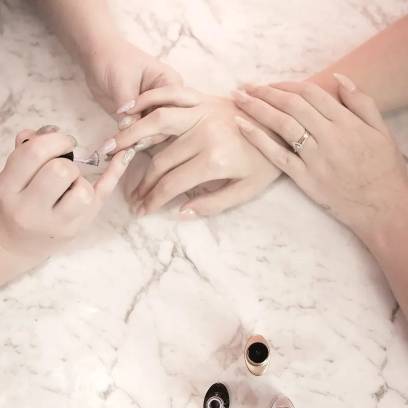 Two pairs of hands over the studio worktop with polish bottles
