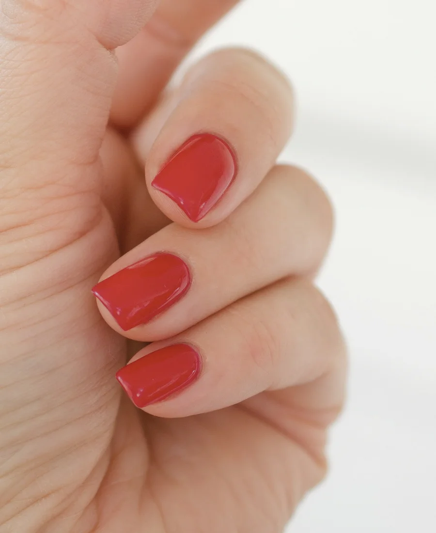 A hand held loosely against a pale background, three polished nails facing the camera