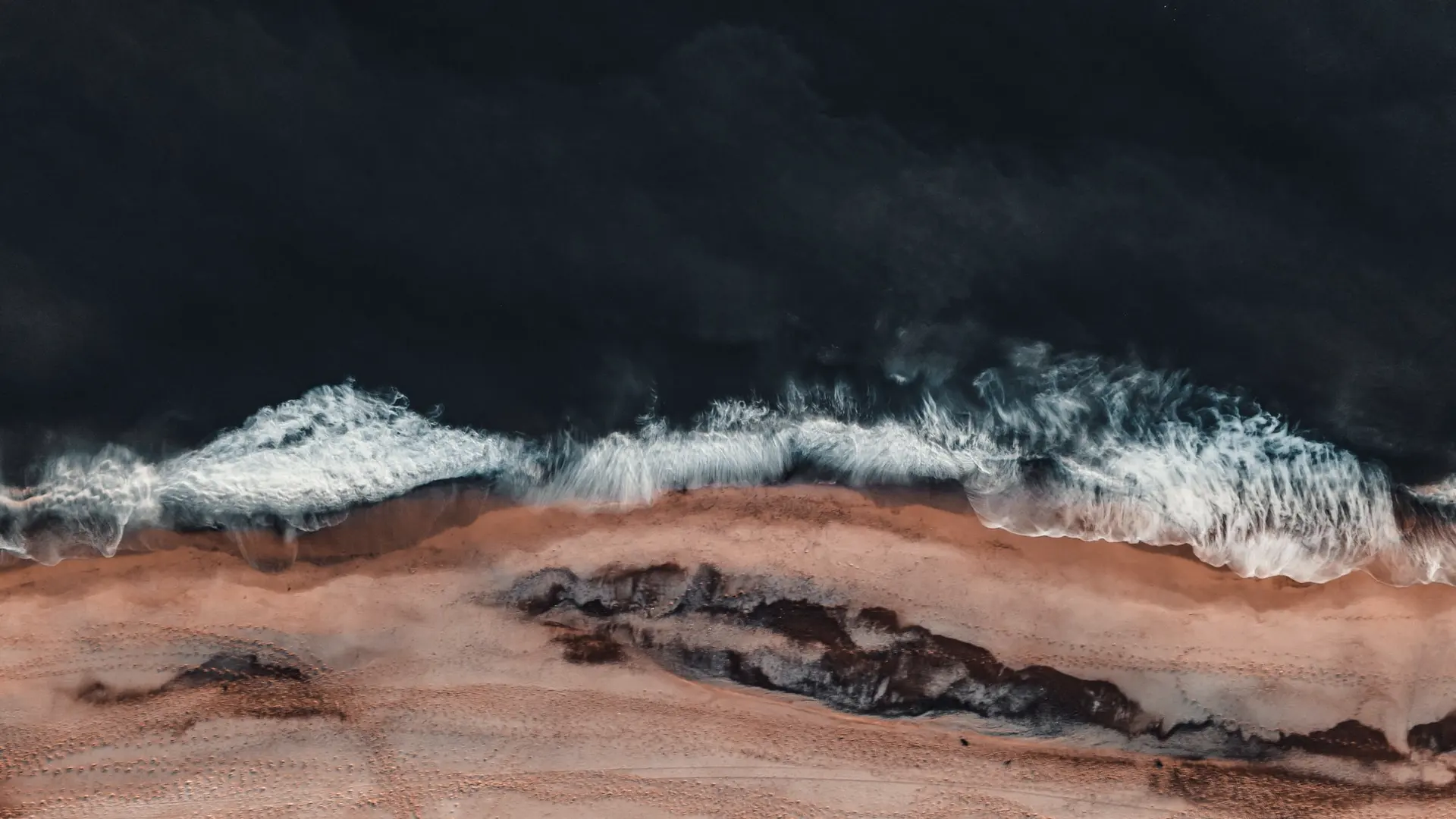 Surf breaking on a dark shore, seen from directly above
