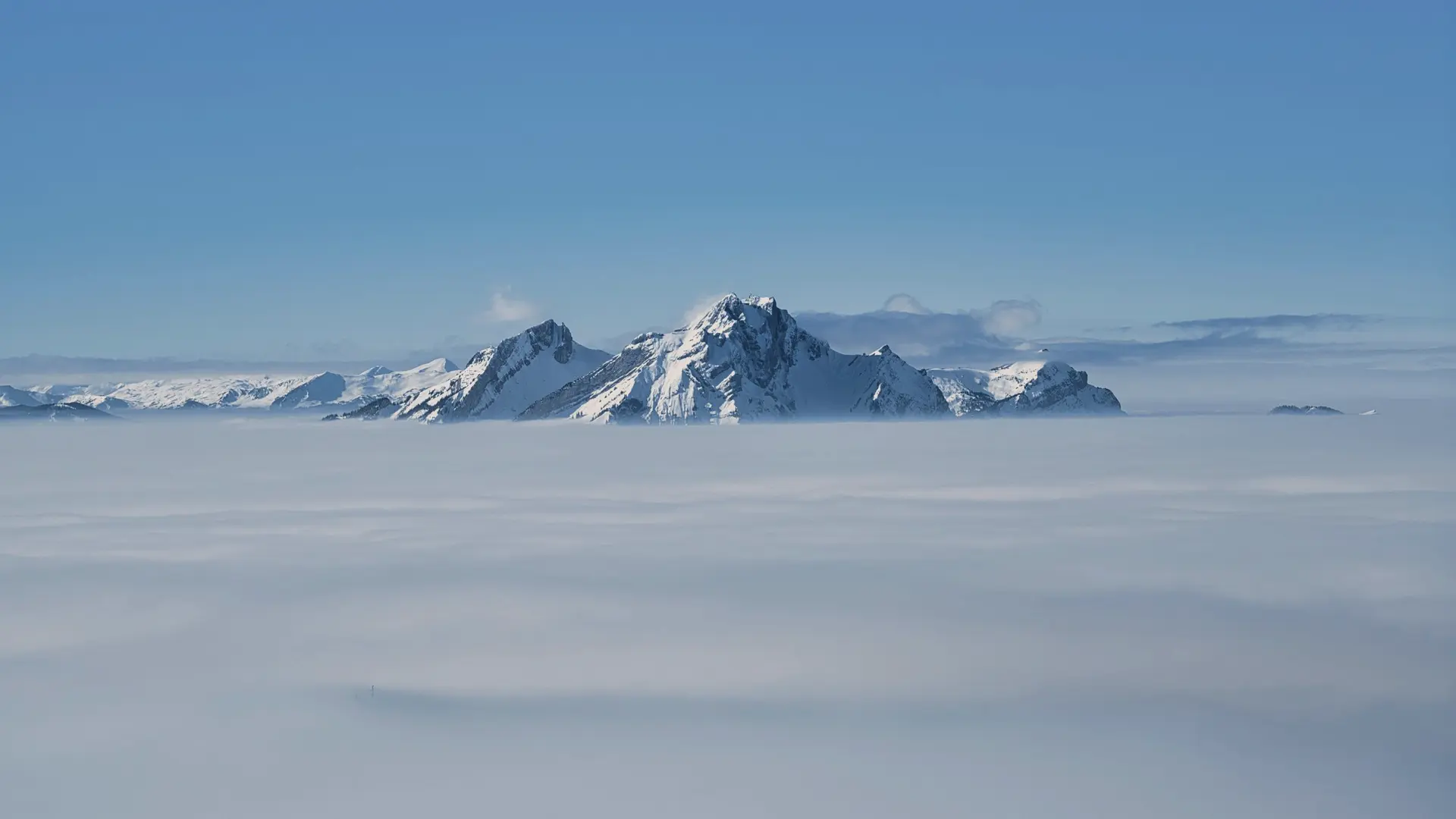 Snow-covered peaks rising through a flat sea of cloud