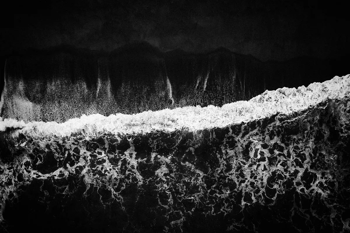 A wave breaking on black sand, seen from above