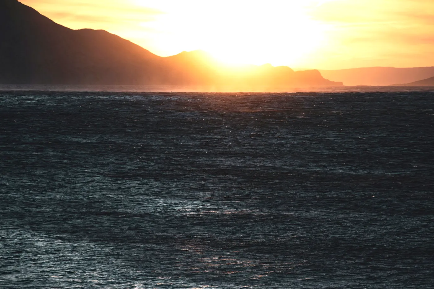 Low sun breaking behind a headland over rough open sea