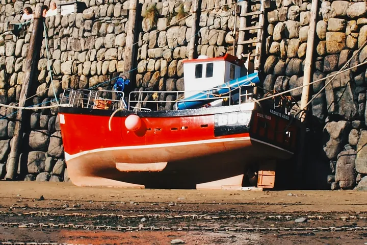 A red fishing boat drawn up against a dry stone harbour wall