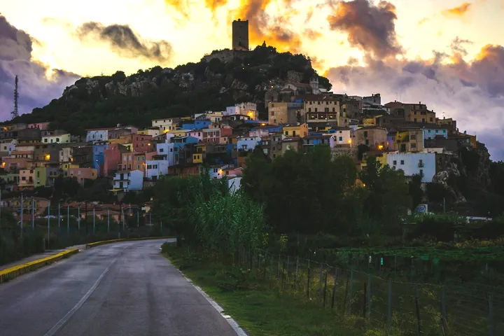 A hill town stacked below a ruined tower under a breaking sky