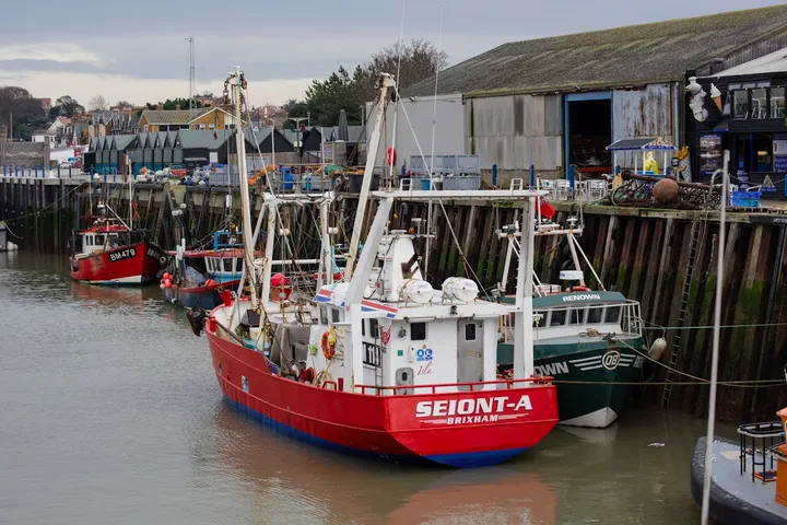 A working trawler tied up alongside a corrugated quayside shed