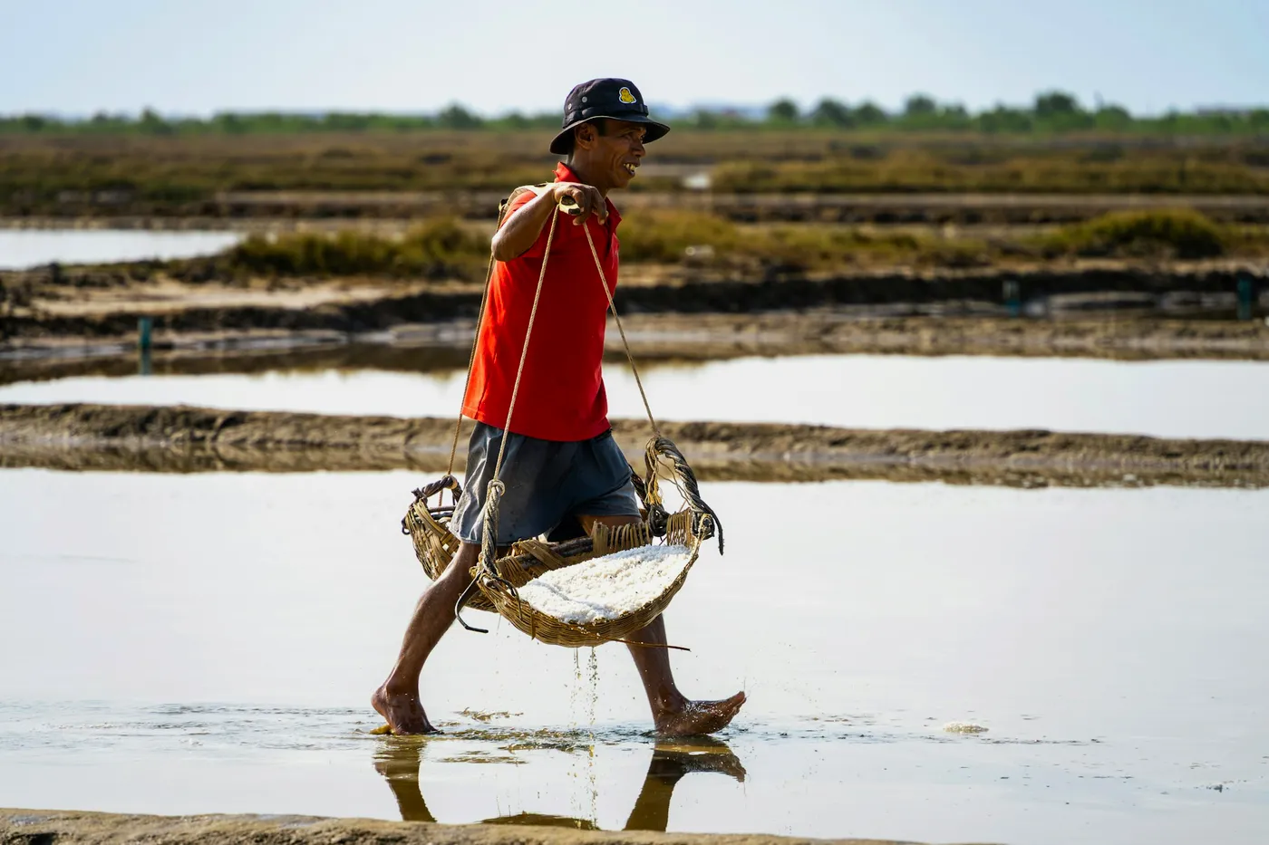 A salt worker carrying a loaded basket across the flooded pans