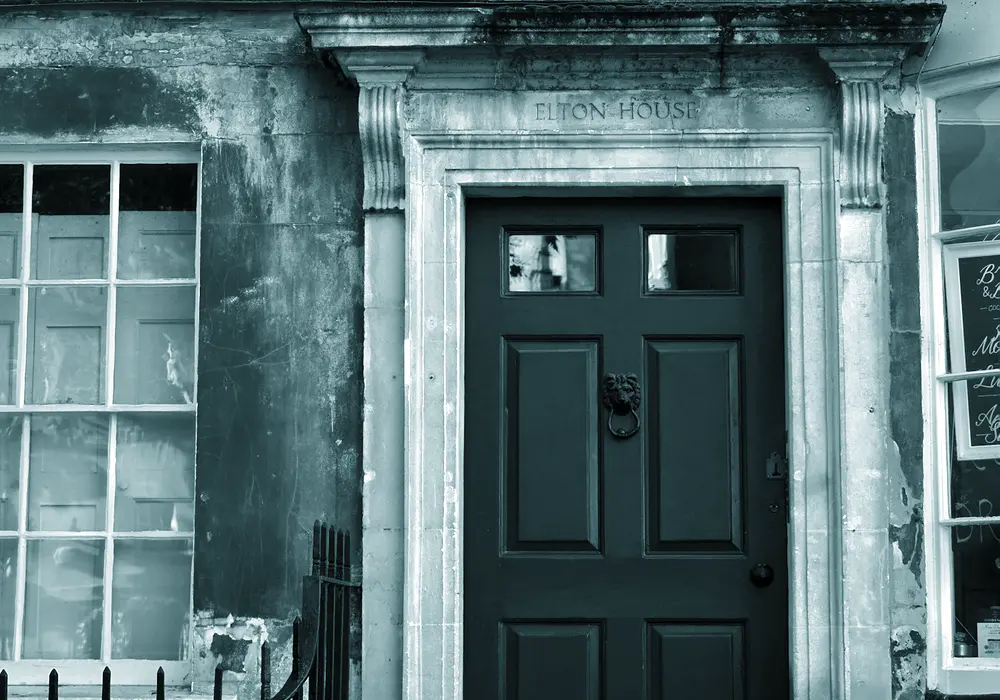 A weathered stone doorcase with a panelled front door