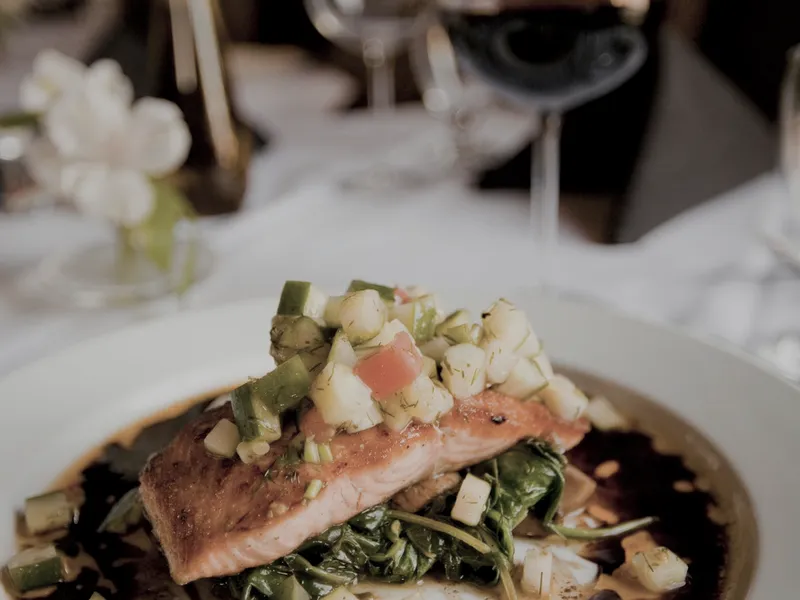 A fillet of cured fish plated with greens in a dark bowl