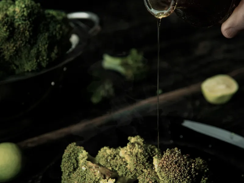 Green vegetables in a dark pan with oil being poured over