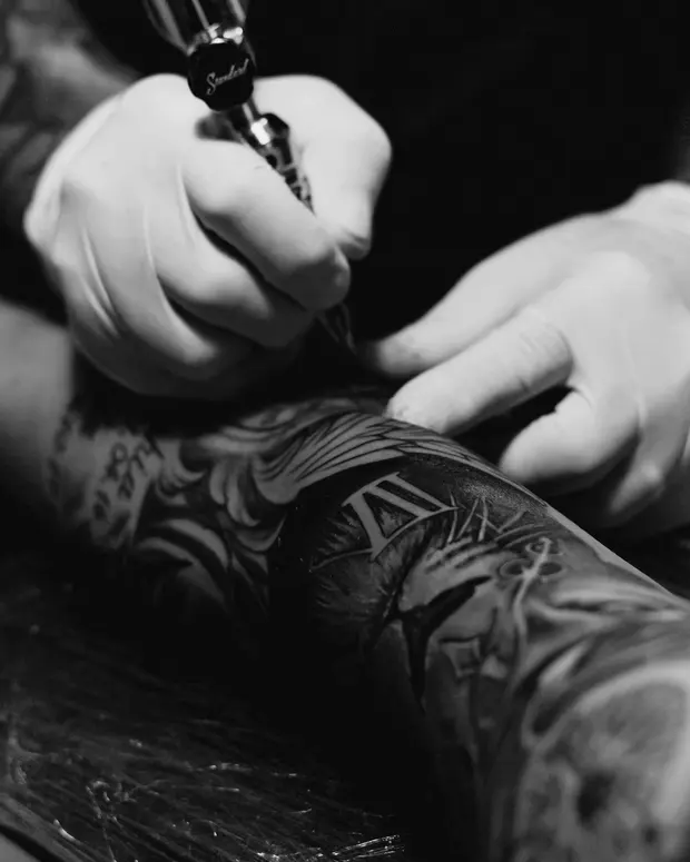 Marek Sowa lining heavy blackwork on a forearm