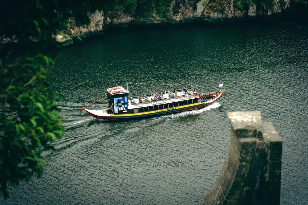 A traditional passenger boat on the Douro between steep, terraced green banks