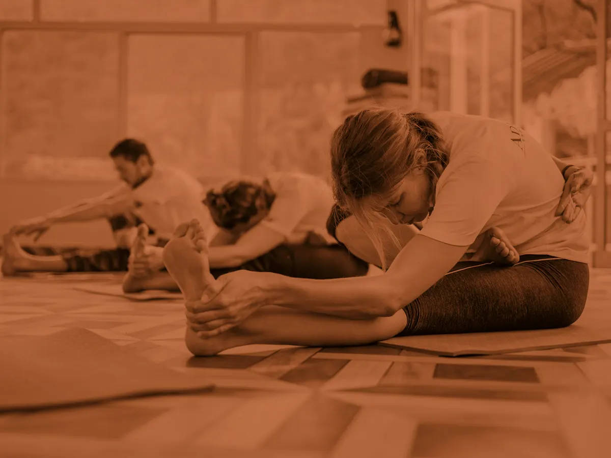 A teacher adjusting a student in a seated forward fold during a class